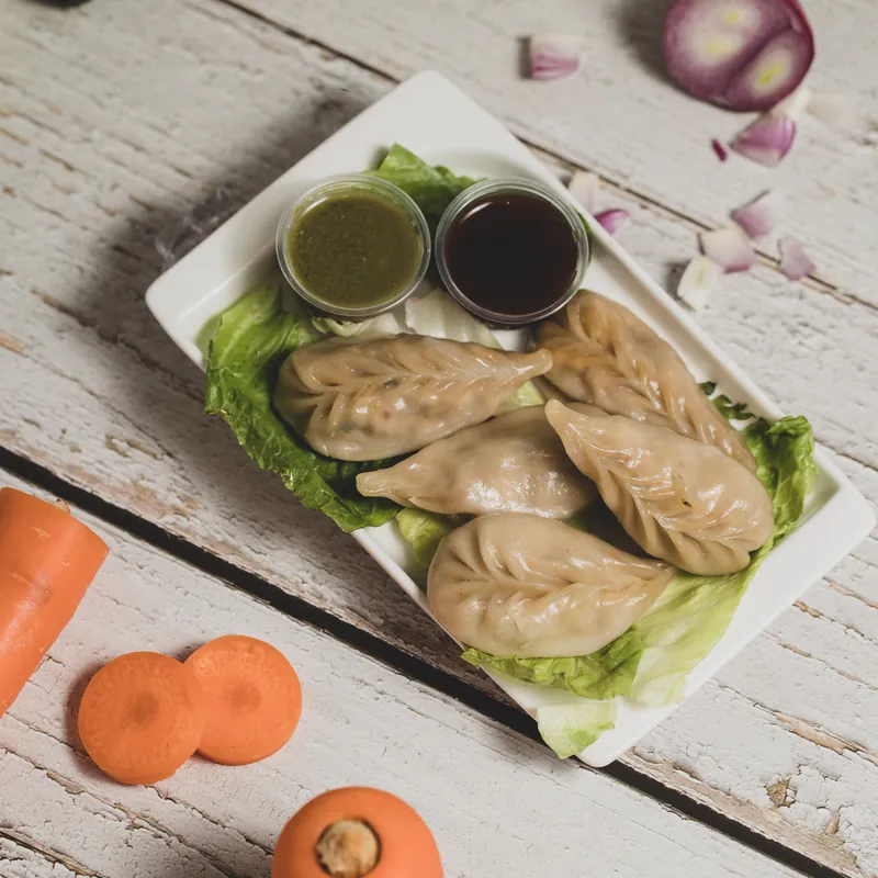 Momos on a lettuce-lined plate with two chutneys