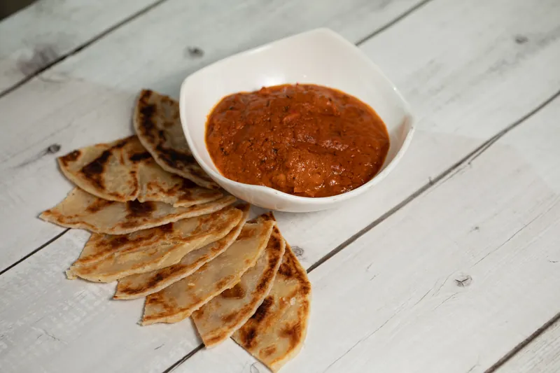 Folded parathas fanned beside a bowl of spiced red gravy